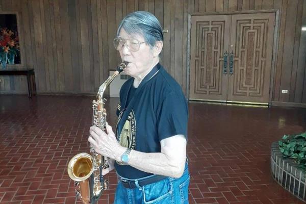 Older Adult standing in a room playing saxophone
