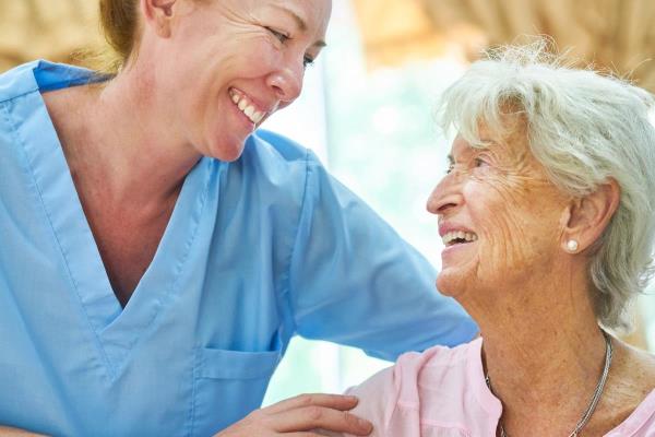 A caregiver and client smile while the caregiver hugs and helps the client, representing professional caregiving.