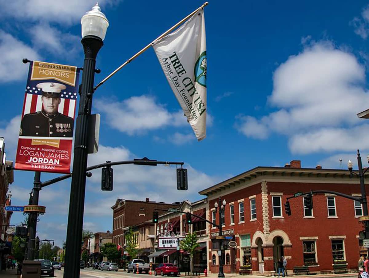 Photo of light post in downtown Westerville, OH with Arbor Day flag and military honor banner. Red brick buildings in the background, a place when Home Instead could provide senior care