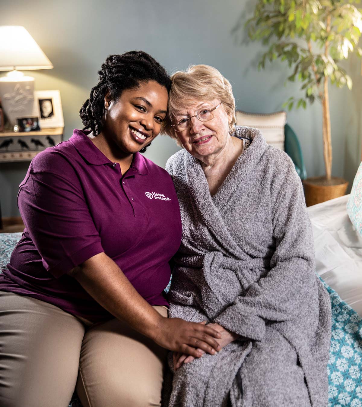 Home Instead CAREGiver and senior sitting on bed smiling